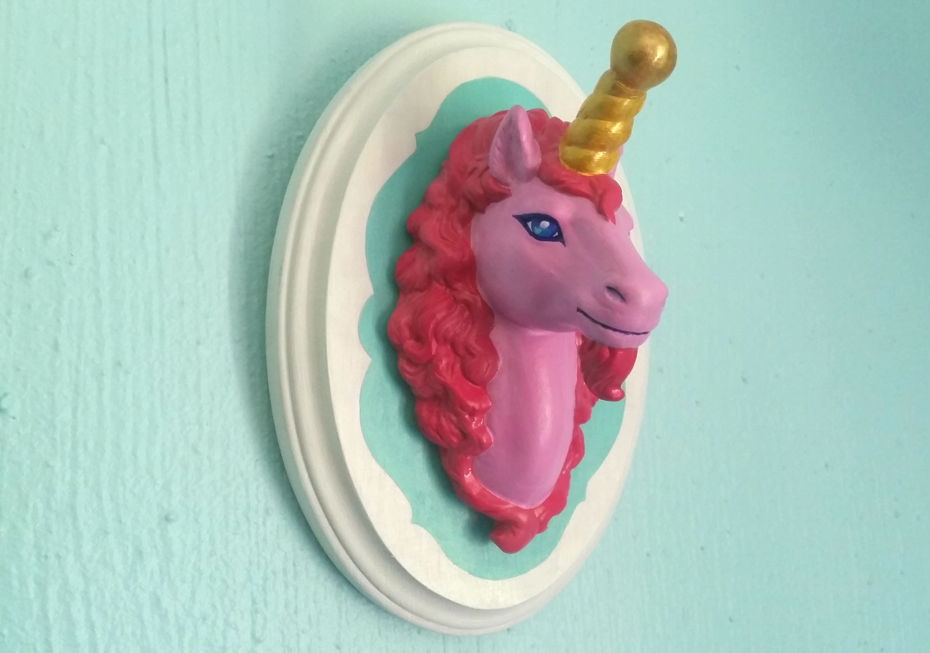 Pink unicorn head mounted on a teal wall.
